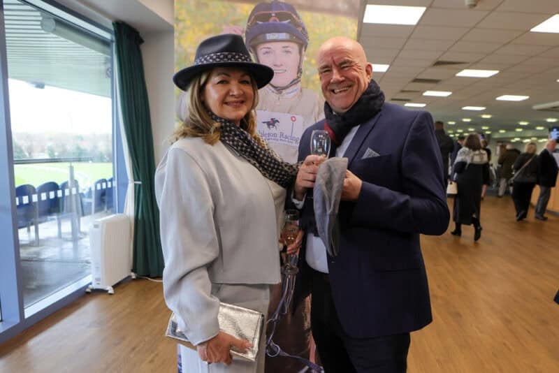 A couple in front of a picture of a Hollie Doyle picture at Doncaster owners day